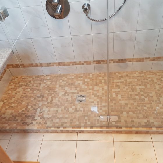 fast bodenenbe Dusche mit kleiner Stufe, extrabreitem Eingang und rutschhemmender Mosaik-Verfliesung in freundlichen Brauntönen 